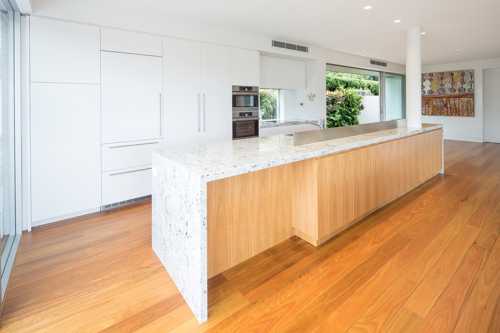 Large contemporary galley eat-in kitchen in Sydney with an integrated sink, light wood cabinets, quartz benchtops, glass sheet splashback and stainless steel appliances.
