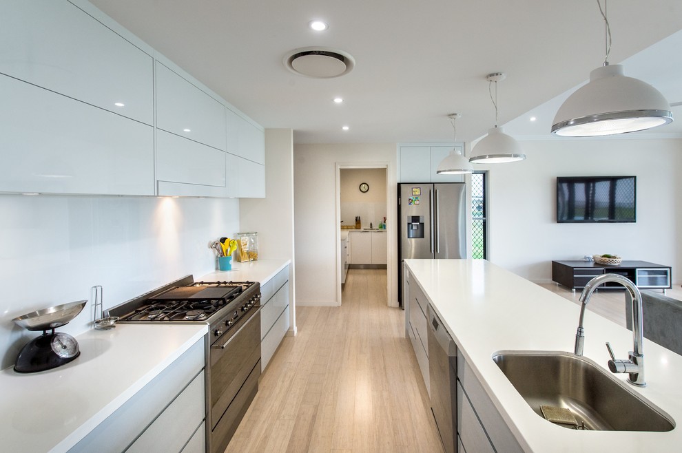 Contemporary galley open plan kitchen in Brisbane with an undermount sink, flat-panel cabinets, white cabinets, stainless steel appliances, light hardwood floors and with island.