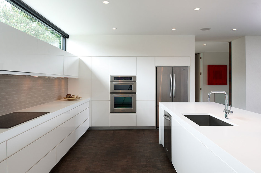 Photo of a mid-sized modern l-shaped open plan kitchen in Minneapolis with stainless steel appliances, an undermount sink, flat-panel cabinets, white cabinets, solid surface benchtops, beige splashback, stone tile splashback, dark hardwood floors and with island.