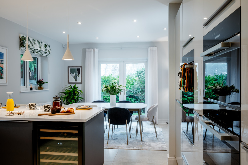 This is an example of a mid-sized contemporary l-shaped open plan kitchen in Surrey with a single-bowl sink, flat-panel cabinets, green cabinets, quartzite benchtops, white splashback, engineered quartz splashback, panelled appliances, porcelain floors, grey floor and white benchtop.