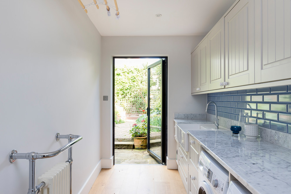 Photo of a mid-sized modern galley dedicated laundry room in London with a drop-in sink, recessed-panel cabinets, grey cabinets, marble benchtops, grey walls, medium hardwood floors, a side-by-side washer and dryer and brown floor.