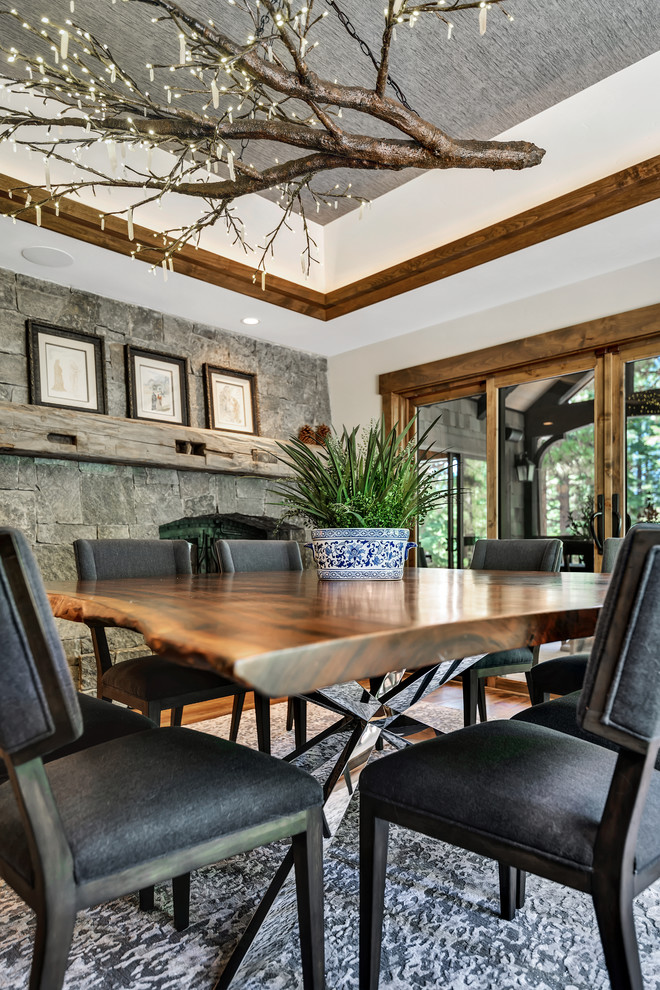 Example of a mid-sized mountain style medium tone wood floor and brown floor enclosed dining room design with gray walls, a two-sided fireplace and a stone fireplace