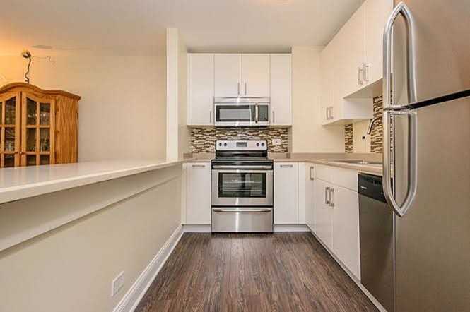 Example of a mid-sized transitional single-wall medium tone wood floor and brown floor open concept kitchen design in Chicago with white cabinets, multicolored backsplash, stainless steel appliances, a peninsula, a drop-in sink, flat-panel cabinets, granite countertops and ceramic backsplash