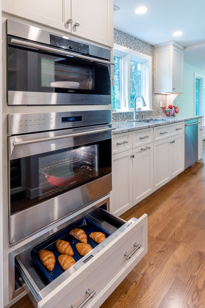 Kitchen photo in Boston with white cabinets, mosaic tile backsplash, stainless steel appliances and an island