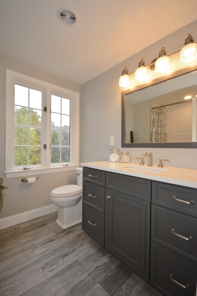 Design ideas for a mid-sized arts and crafts bathroom in Other with beaded inset cabinets, grey cabinets, an alcove tub, a shower/bathtub combo, a two-piece toilet, white tile, subway tile, grey walls, porcelain floors, an undermount sink, engineered quartz benchtops, beige floor, a shower curtain and white benchtops.