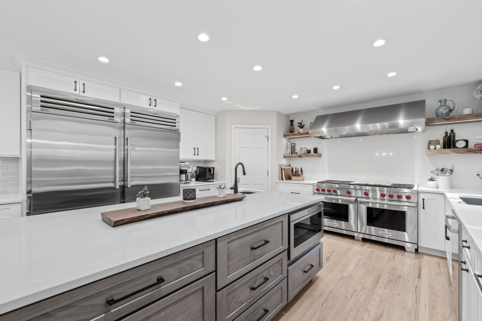 Inspiration for a large transitional u-shaped light wood floor and multicolored floor eat-in kitchen remodel with a single-bowl sink, shaker cabinets, white cabinets, quartz countertops, white backsplash, quartz backsplash, stainless steel appliances, an island and white countertops