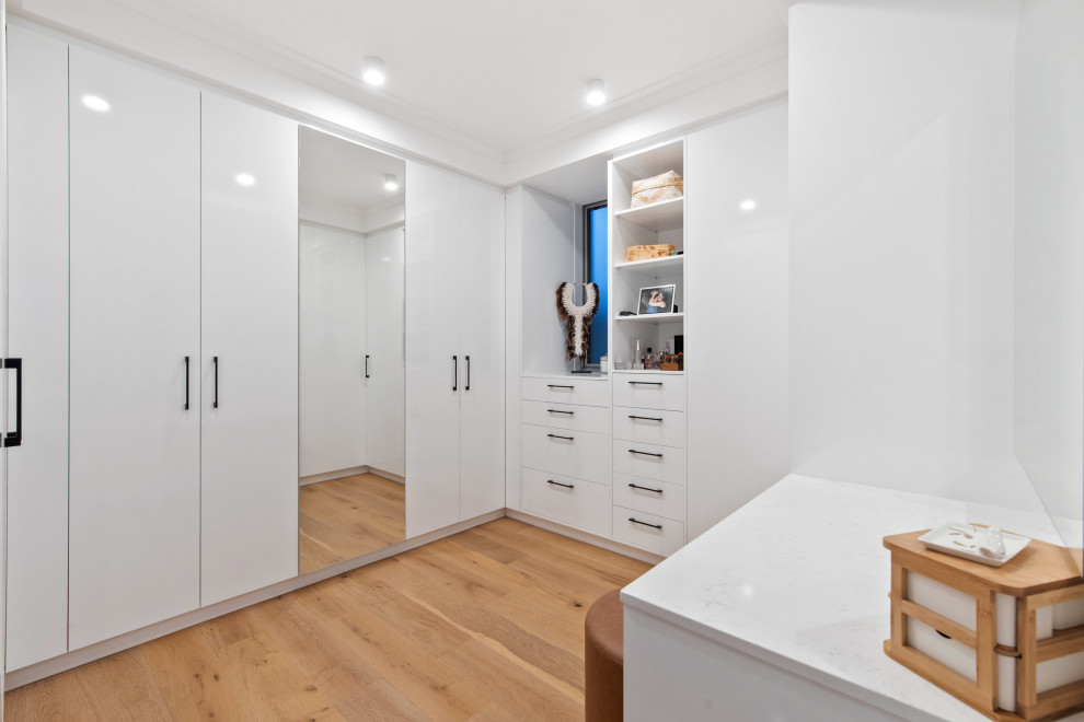 Large contemporary gender-neutral dressing room in Perth with flat-panel cabinets, white cabinets, medium hardwood floors and beige floor.