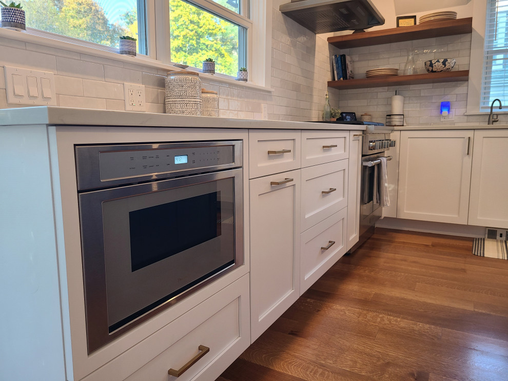 Example of a large transitional u-shaped medium tone wood floor and brown floor eat-in kitchen design in Boston with an undermount sink, recessed-panel cabinets, white cabinets, white backsplash, subway tile backsplash, stainless steel appliances, an island and white countertops
