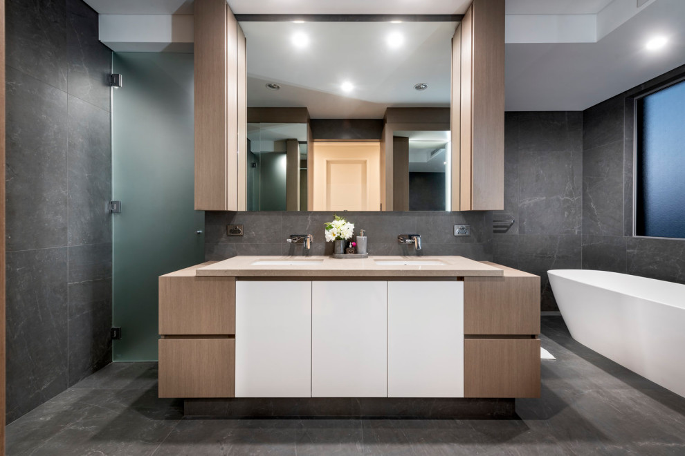 Modern bathroom in Perth with flat-panel cabinets, white cabinets, a freestanding tub, gray tile, grey walls, an undermount sink, grey floor and beige benchtops.