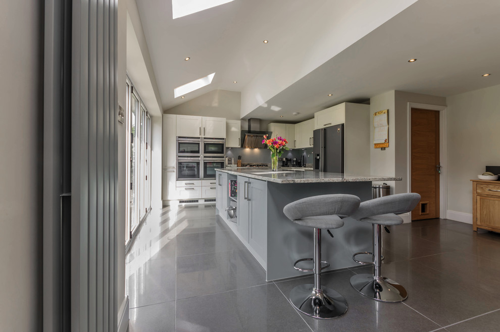 This is an example of a large contemporary l-shaped eat-in kitchen in Other with a single-bowl sink, shaker cabinets, blue cabinets, granite benchtops, grey splashback, glass sheet splashback, stainless steel appliances, porcelain floors and with island.
