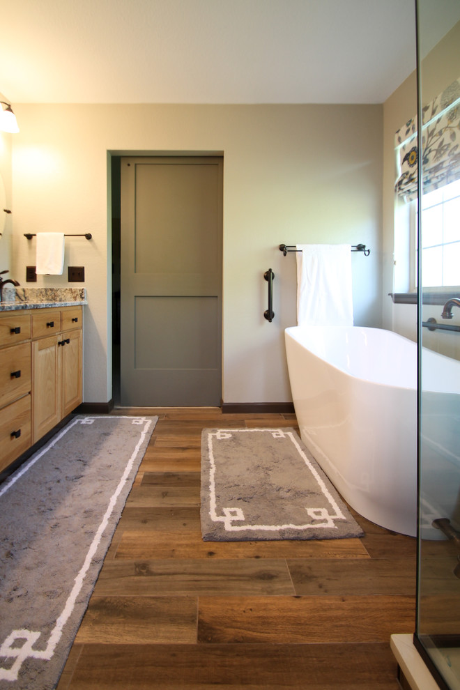 Mid-sized traditional master bathroom in Denver with raised-panel cabinets, light wood cabinets, a freestanding tub, a corner shower, a one-piece toilet, beige tile, porcelain tile, green walls, porcelain floors, an undermount sink, granite benchtops, brown floor and a hinged shower door.