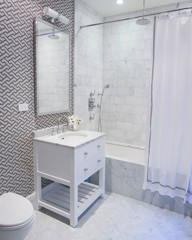 Photo of a contemporary bathroom in New York with an undermount sink, flat-panel cabinets, white cabinets, marble benchtops, an alcove tub, a shower/bathtub combo, a two-piece toilet, white tile, stone tile, white walls, marble floors and a shower curtain.