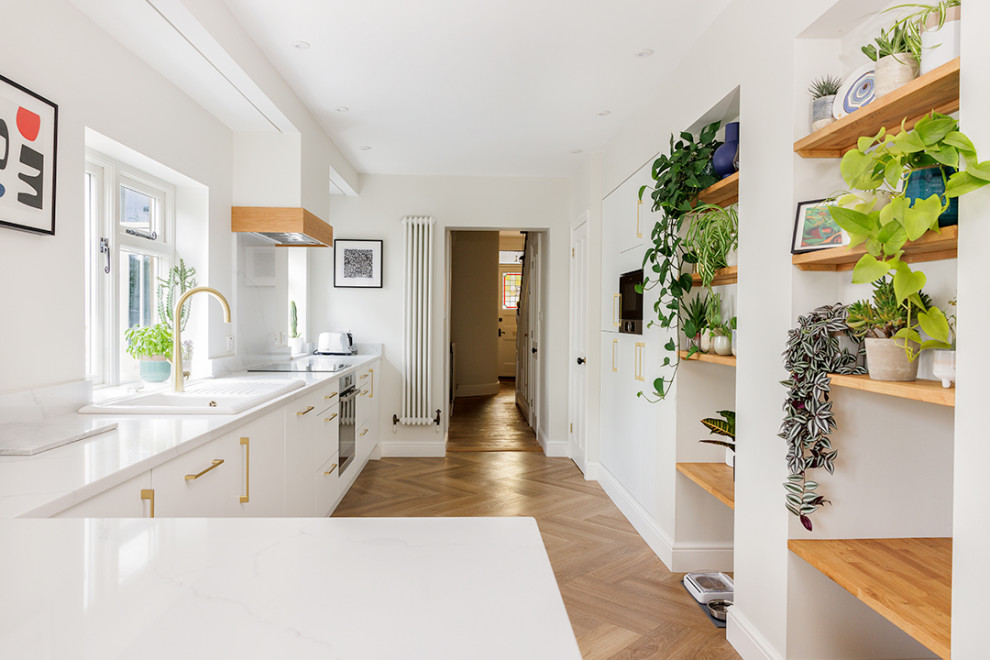 Inspiration for a medium sized modern grey and white galley kitchen/diner with flat-panel cabinets, white cabinets, engineered stone countertops, beige splashback, engineered quartz splashback, black appliances, a breakfast bar, white worktops and feature lighting.