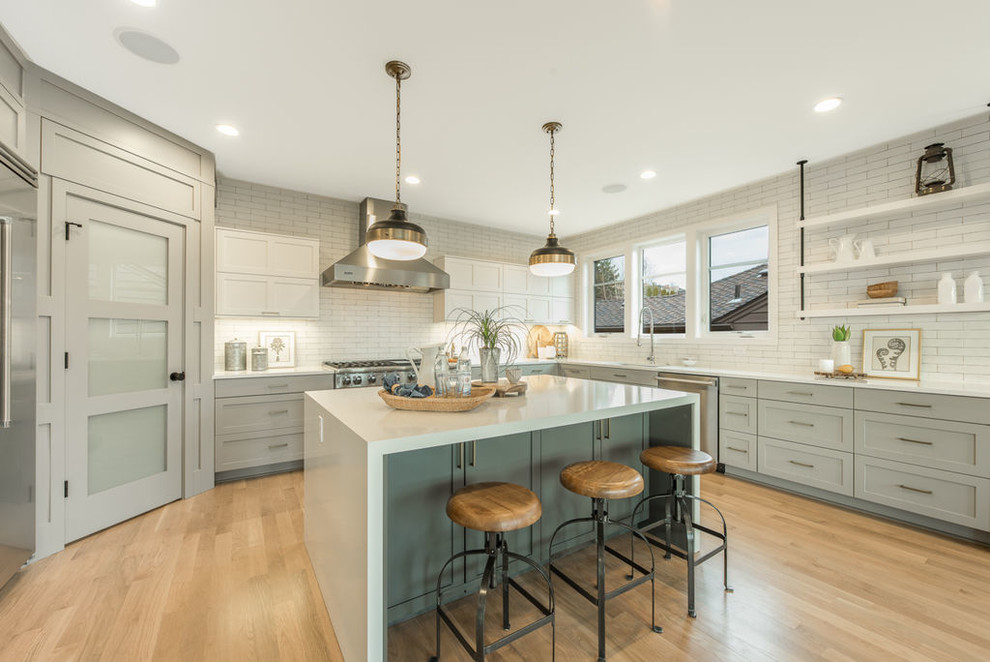 Design ideas for a mid-sized transitional u-shaped open plan kitchen in Seattle with an undermount sink, shaker cabinets, grey cabinets, solid surface benchtops, white splashback, subway tile splashback, stainless steel appliances, light hardwood floors, with island and beige floor.