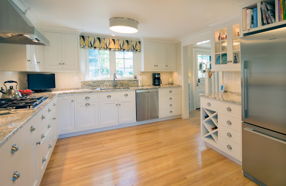 Photo of a mid-sized beach style u-shaped separate kitchen in New York with an undermount sink, beaded inset cabinets, white cabinets, granite benchtops, beige splashback, stainless steel appliances, light hardwood floors and no island.