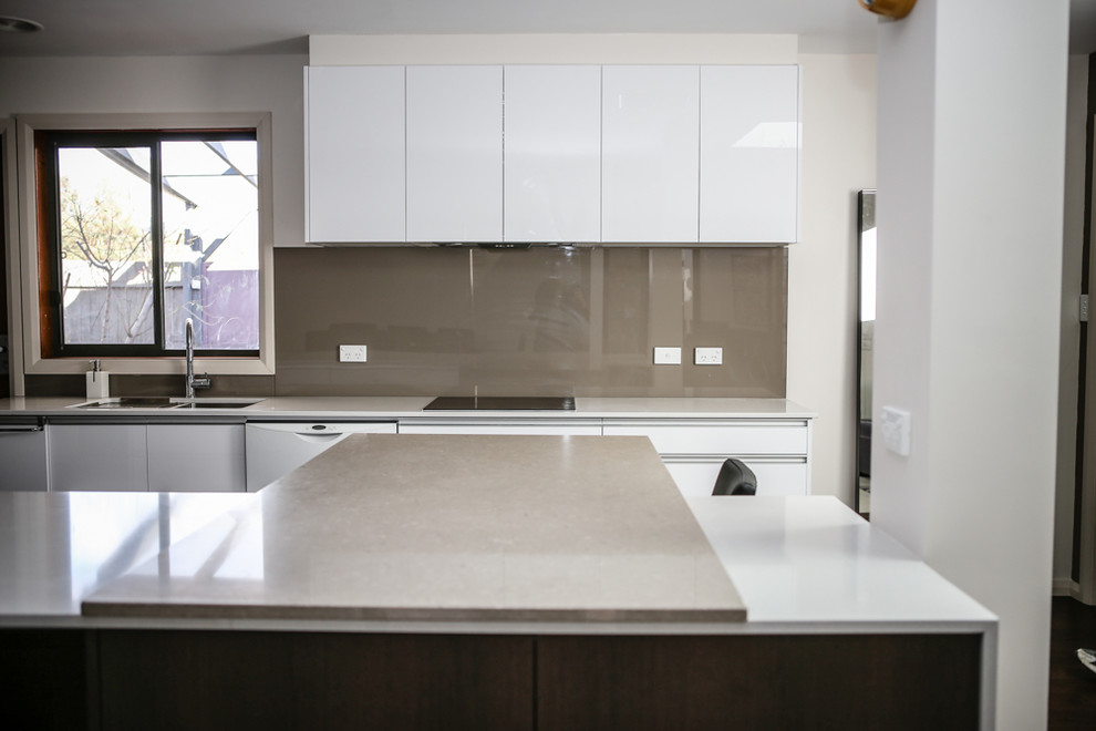 This is an example of a large contemporary l-shaped eat-in kitchen with an undermount sink, flat-panel cabinets, white cabinets, quartz benchtops, white splashback, glass sheet splashback, white appliances, dark hardwood floors and multiple islands.