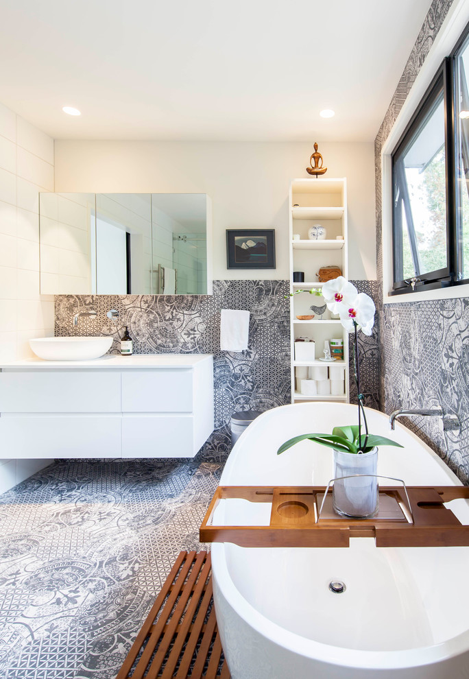 Photo of a large contemporary master bathroom in Melbourne with white cabinets, a freestanding tub, a corner shower, a two-piece toilet, black and white tile, ceramic tile, white walls, ceramic floors, a vessel sink, solid surface benchtops, black floor, a hinged shower door, white benchtops and flat-panel cabinets.