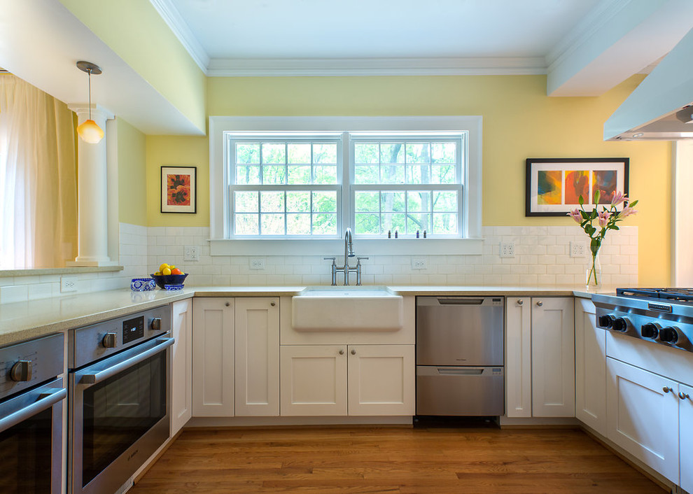 Photo of a mid-sized traditional u-shaped open plan kitchen in Atlanta with a farmhouse sink, shaker cabinets, white cabinets, white splashback, subway tile splashback, stainless steel appliances, medium hardwood floors, a peninsula and brown floor.
