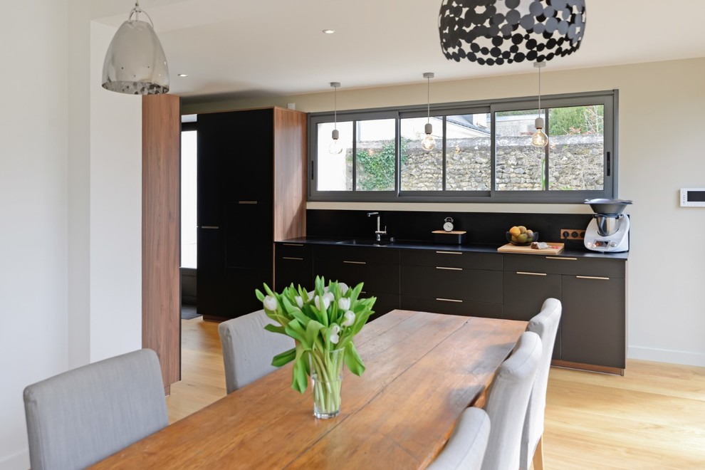 Inspiration for a mid-sized contemporary galley open plan kitchen in Angers with an integrated sink, flat-panel cabinets, black cabinets, laminate benchtops, black splashback, stainless steel appliances, light hardwood floors, no island and black benchtop.