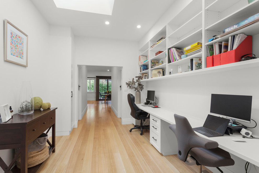 Photo of a small contemporary study room in Melbourne with white walls, light hardwood floors, a built-in desk and beige floor.