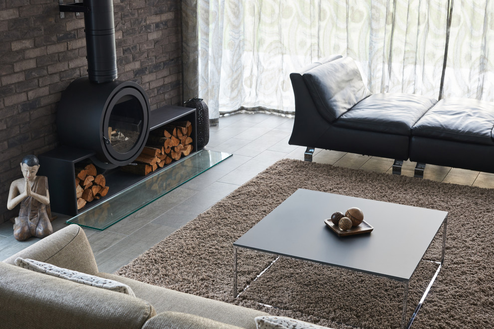 Contemporary living room in Devon with black walls, ceramic floors, a hanging fireplace, a brick fireplace surround and brown floor.