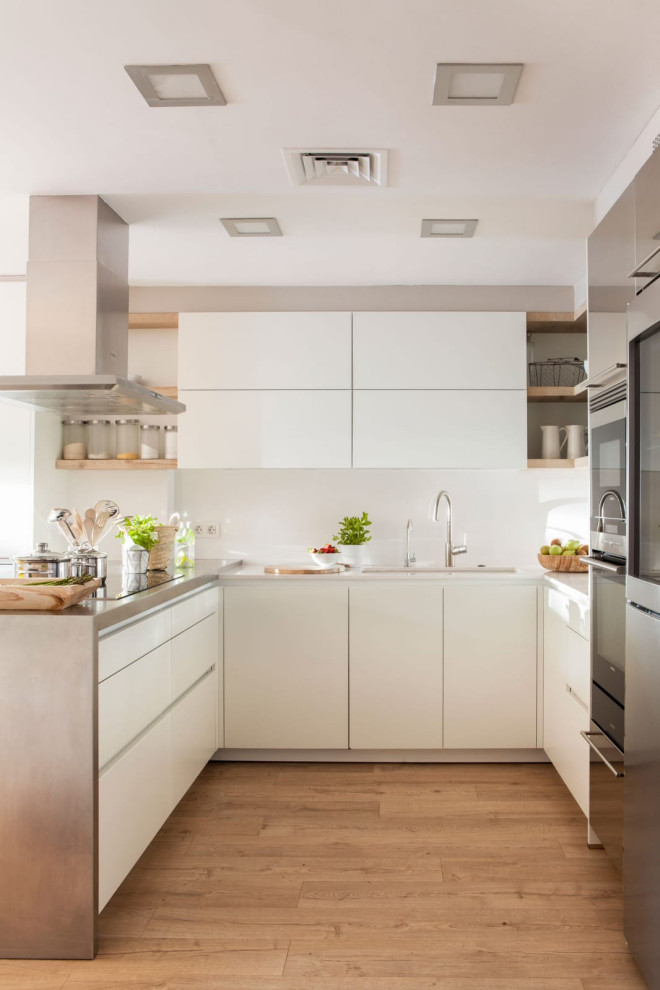 Bild på ett funkis grå grått u-kök, med en undermonterad diskho, släta luckor, vita skåp, rostfria vitvaror, ljust trägolv, en halv köksö och beiget golv
