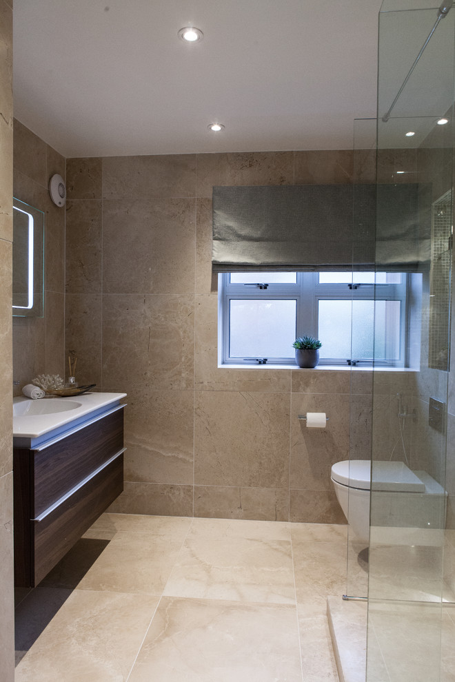 Photo of a mid-sized contemporary master bathroom in Hampshire with flat-panel cabinets, dark wood cabinets, an open shower, a wall-mount toilet, beige tile, limestone, beige walls, limestone floors, a wall-mount sink, solid surface benchtops, beige floor and an open shower.