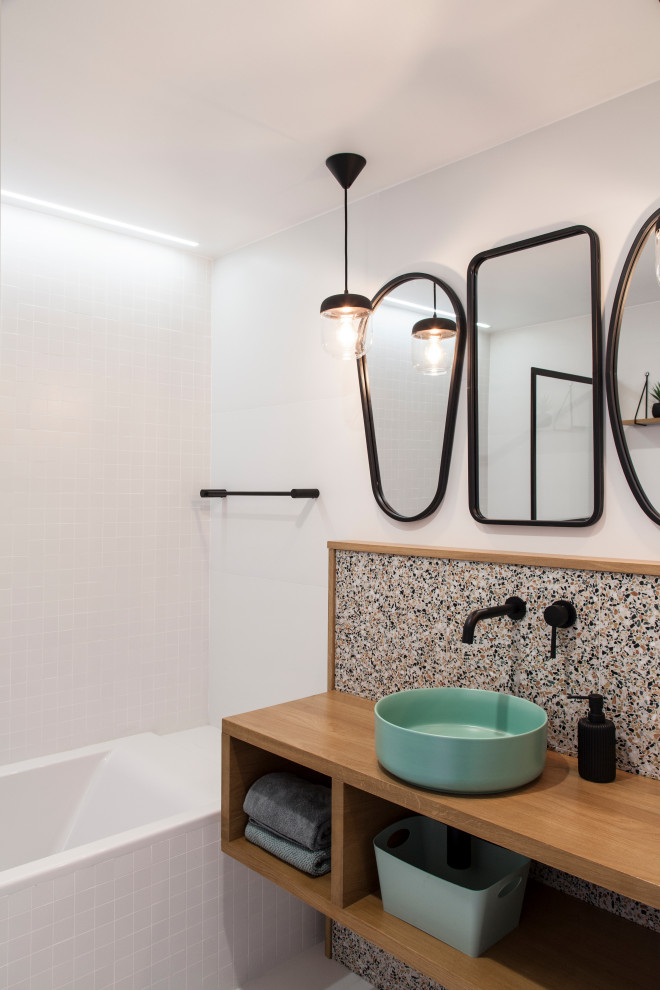 Photo of a small contemporary master bathroom in Other with open cabinets, light wood cabinets, an undermount tub, a wall-mount toilet, multi-coloured tile, ceramic tile, white walls, ceramic floors, a vessel sink, wood benchtops and white floor.