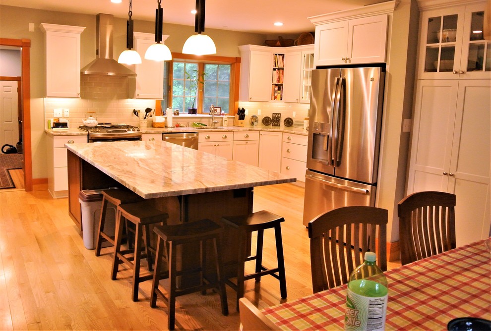 Example of a transitional light wood floor kitchen design in Boston with an undermount sink, shaker cabinets, white cabinets, quartzite countertops, white backsplash, subway tile backsplash, stainless steel appliances and an island