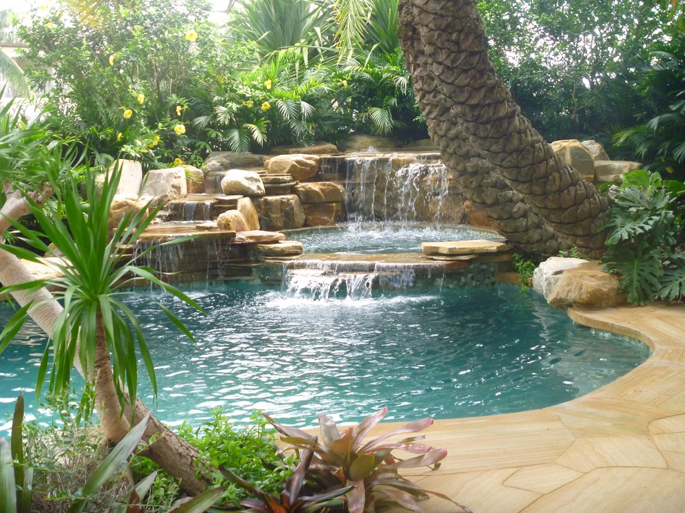 Tropical backyard custom-shaped natural pool in Miami with a water feature and natural stone pavers.