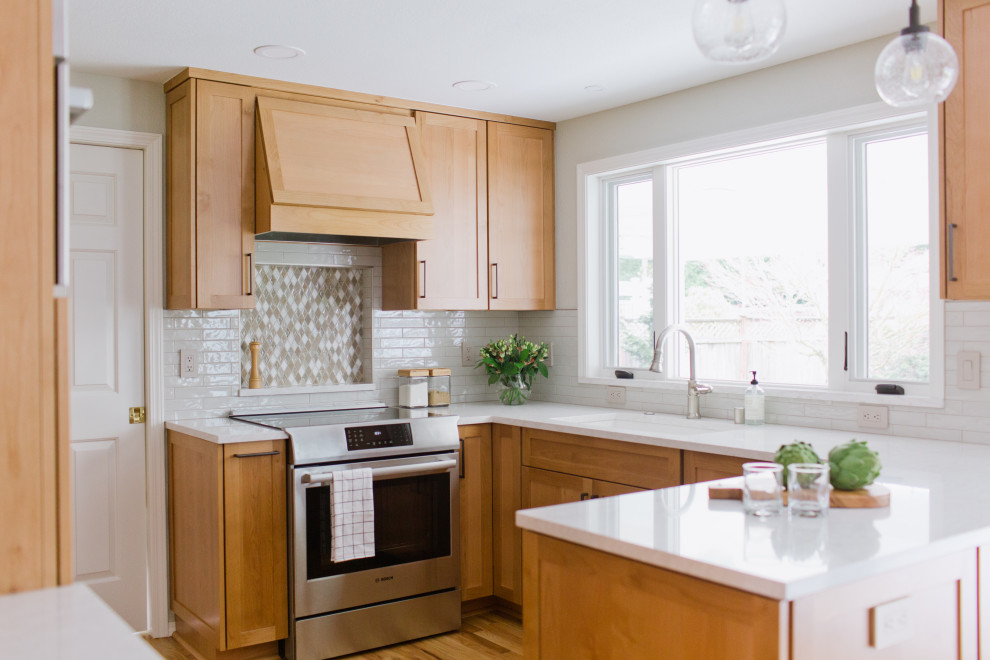 Transitional u-shaped kitchen in Seattle with an undermount sink, shaker cabinets, medium wood cabinets, white splashback, stainless steel appliances, medium hardwood floors, a peninsula, brown floor and white benchtop.