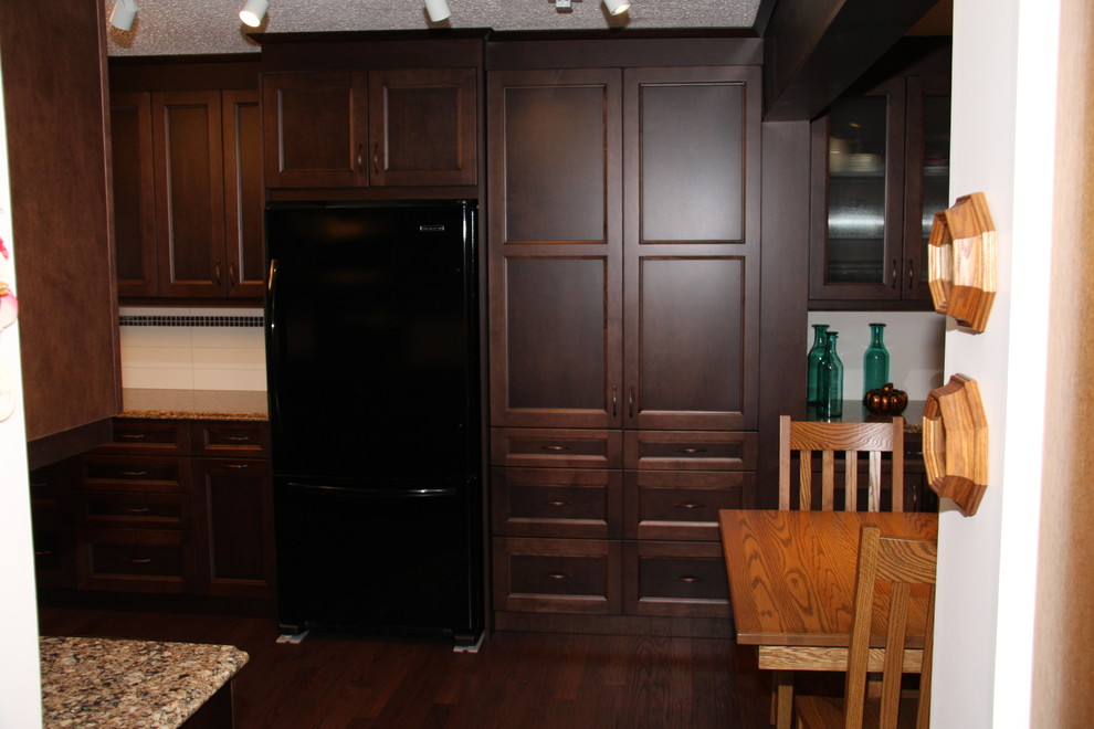 Example of a mid-sized classic u-shaped medium tone wood floor eat-in kitchen design in Edmonton with a farmhouse sink, shaker cabinets, medium tone wood cabinets, granite countertops, white backsplash, subway tile backsplash, black appliances and no island