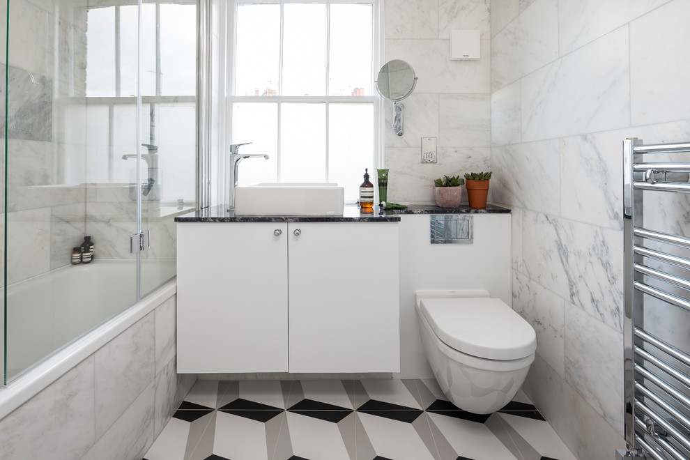 This is an example of a mid-sized transitional bathroom in London with flat-panel cabinets, white cabinets, a drop-in tub, white tile, marble, a vessel sink and multi-coloured floor.