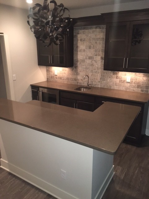 Photo of a large galley seated home bar in Columbus with an undermount sink, glass-front cabinets, dark wood cabinets, beige splashback, stone tile splashback and dark hardwood floors.