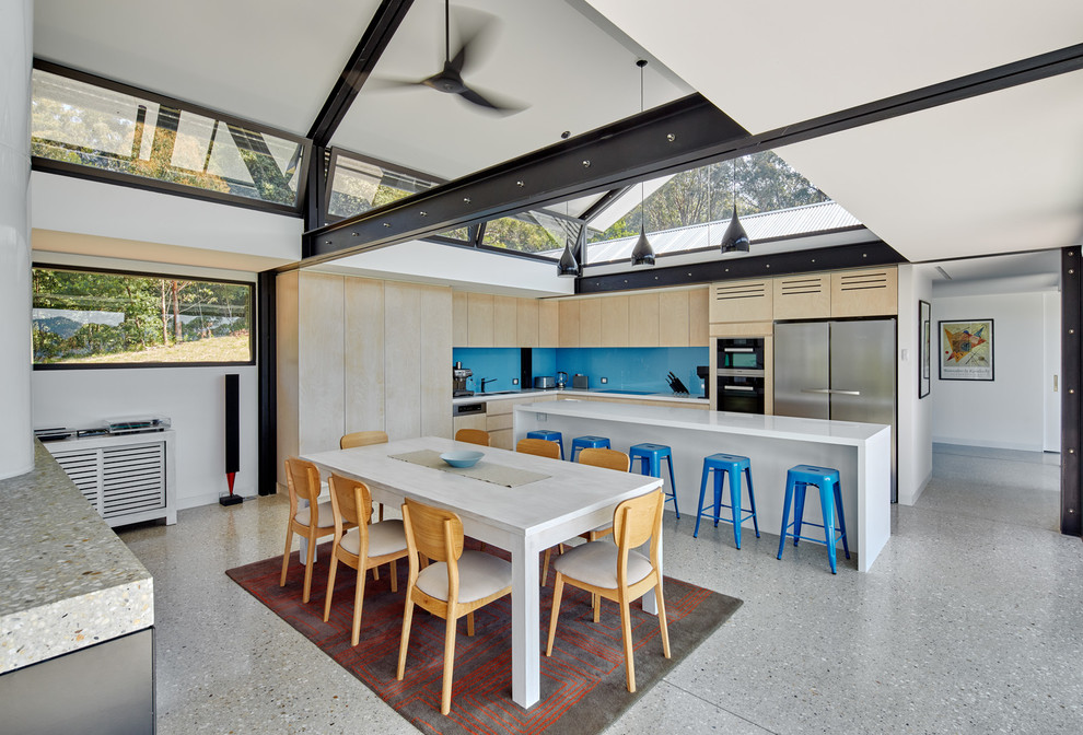 Large contemporary l-shaped eat-in kitchen in Sydney with a double-bowl sink, light wood cabinets, blue splashback, glass sheet splashback, stainless steel appliances, concrete floors, with island, flat-panel cabinets and quartz benchtops.