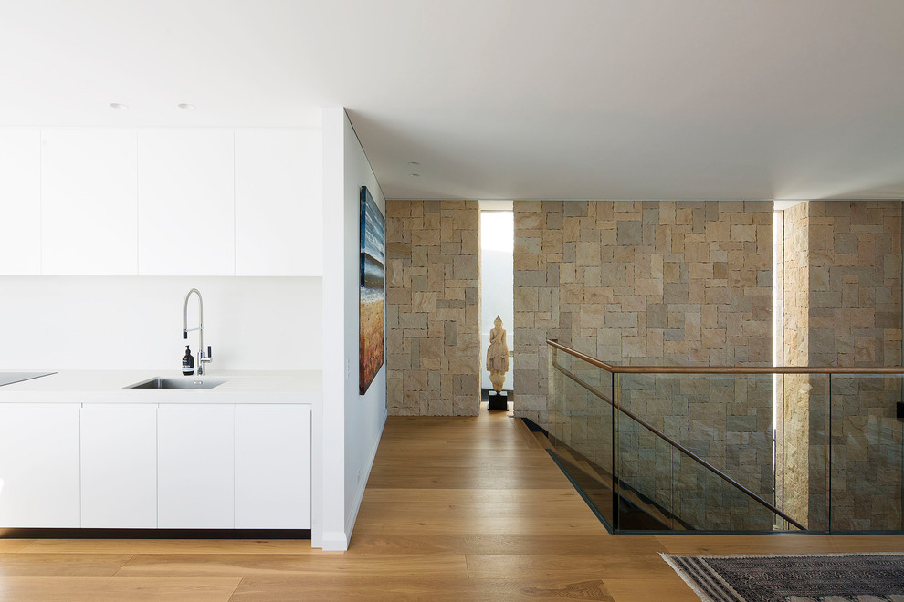 This is an example of a large contemporary galley open plan kitchen in Sydney with flat-panel cabinets, white cabinets, quartz benchtops, white splashback, stone slab splashback, light hardwood floors, with island and white benchtop.