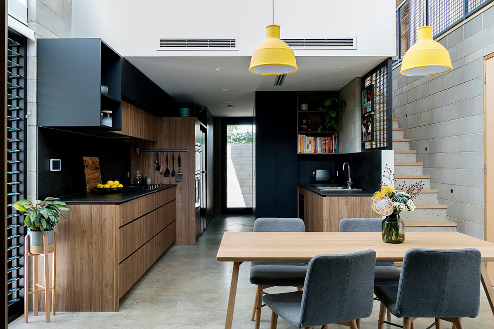 Inspiration for a large modern galley eat-in kitchen in Perth with a double-bowl sink, flat-panel cabinets, medium wood cabinets, tile benchtops, black splashback, porcelain splashback, stainless steel appliances, concrete floors, grey floor and black benchtop.