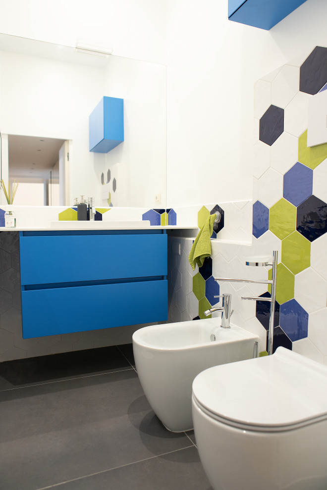 Photo of a small modern family bathroom in Milan with flat-panel cabinets, blue cabinets, a two-piece toilet, green walls, porcelain flooring, a built-in sink, engineered stone worktops, white worktops, a floating vanity unit, green tiles, mosaic tiles, an enclosed toilet, a single sink, a drop ceiling and grey floors.