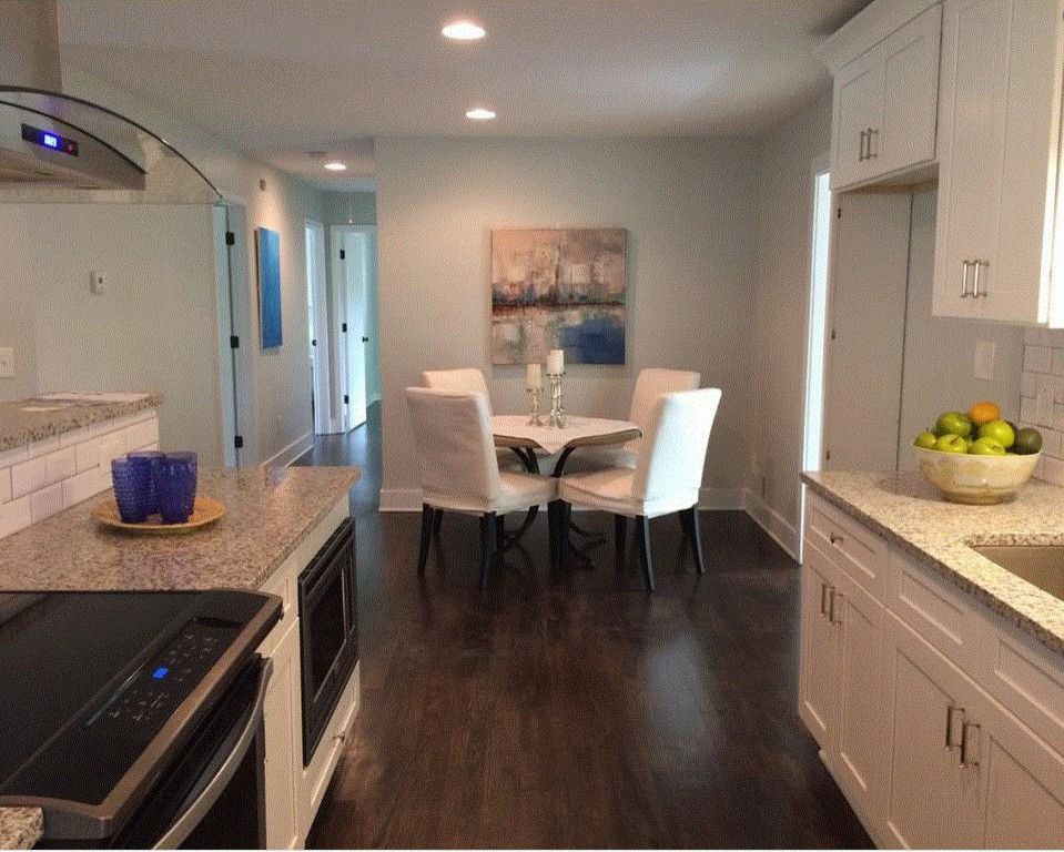 This is an example of a mid-sized arts and crafts eat-in kitchen in Atlanta with a farmhouse sink, shaker cabinets, white cabinets, granite benchtops, white splashback, ceramic splashback, stainless steel appliances, dark hardwood floors, with island, black floor and multi-coloured benchtop.