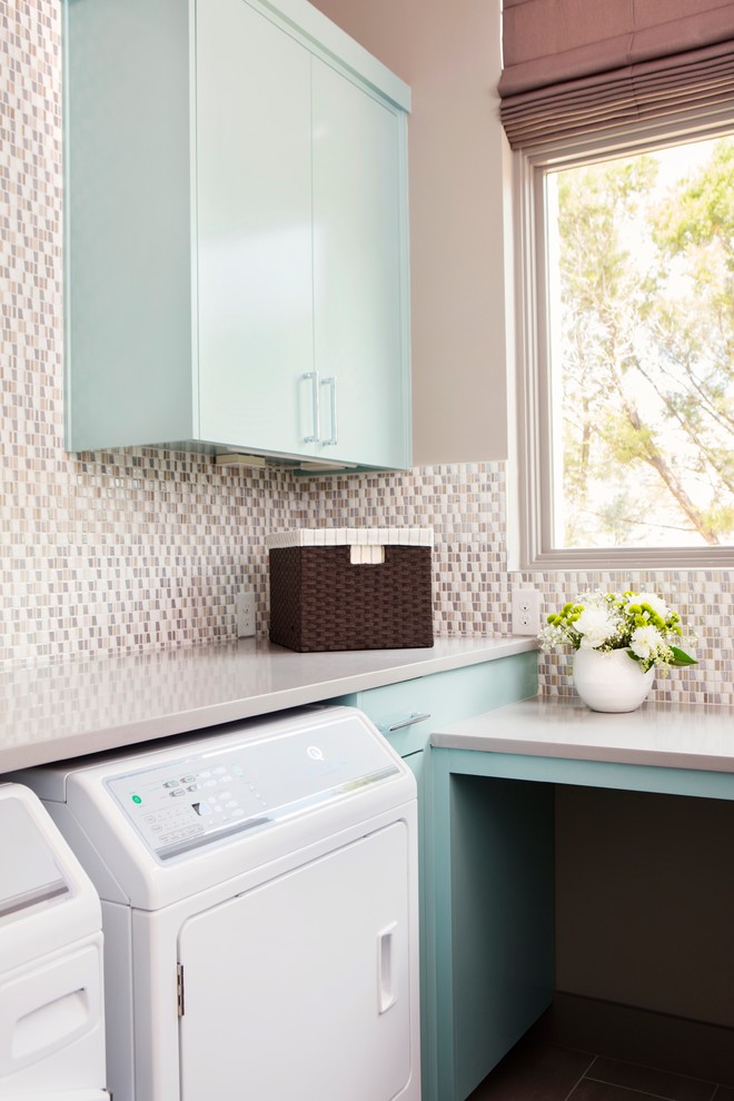 This is an example of a mid-sized transitional l-shaped dedicated laundry room in Austin with an undermount sink, flat-panel cabinets, turquoise cabinets, solid surface benchtops, grey walls, porcelain floors, a side-by-side washer and dryer, brown floor and grey benchtop.