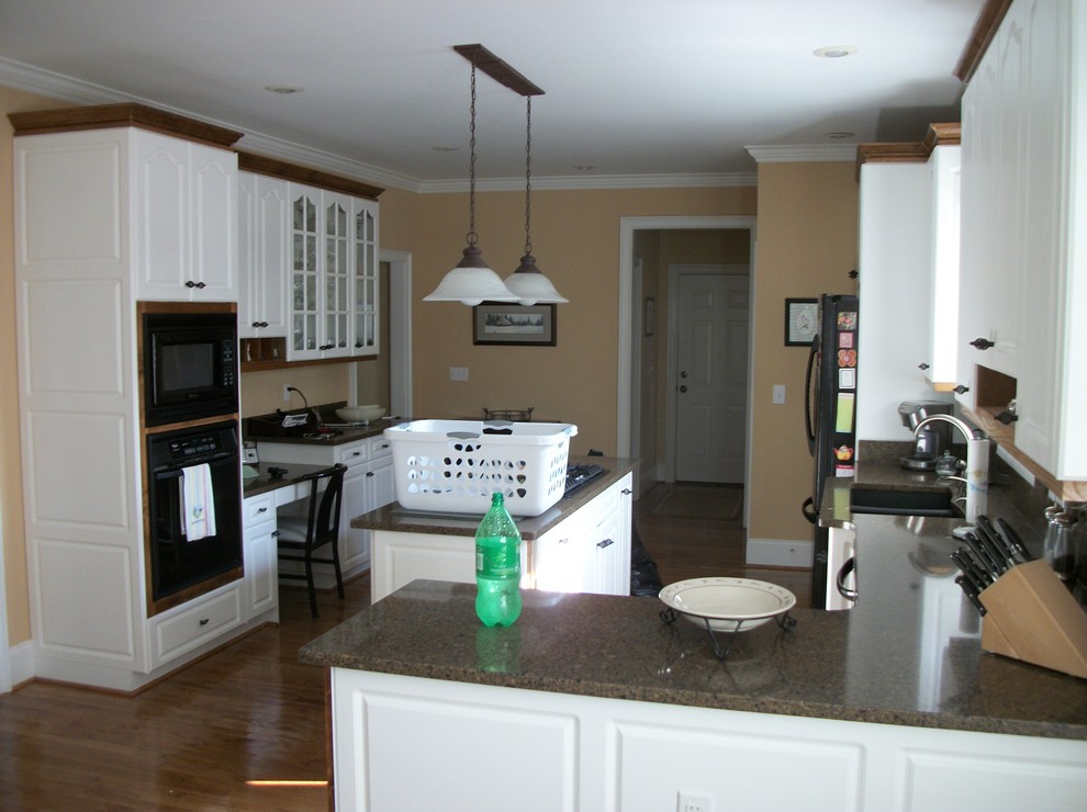 Transitional u-shaped medium tone wood floor kitchen photo with raised-panel cabinets, white cabinets, granite countertops, black appliances and an island