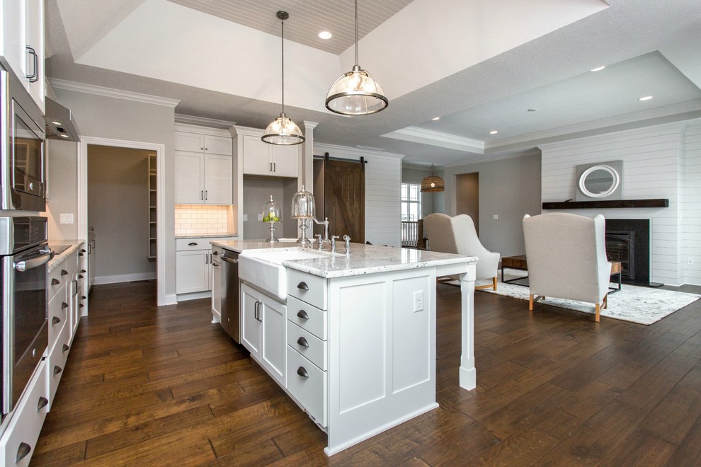 Inspiration for a mid-sized transitional single-wall medium tone wood floor and beige floor open concept kitchen remodel with a farmhouse sink, recessed-panel cabinets, white cabinets, granite countertops, white backsplash, stainless steel appliances, an island and ceramic backsplash