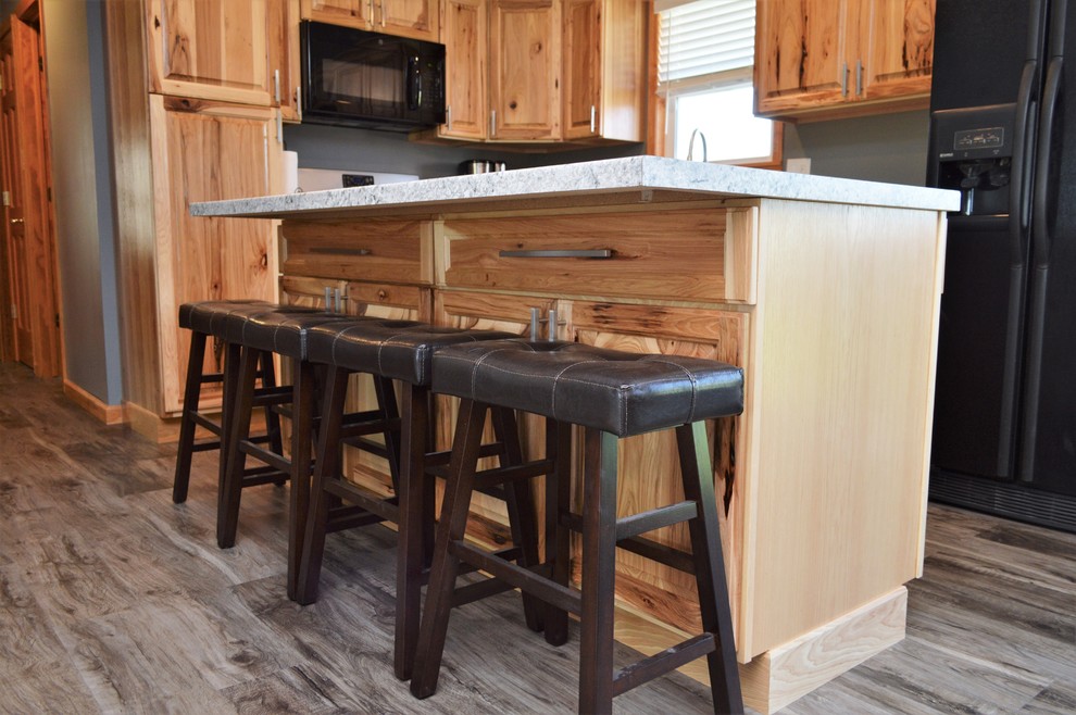 This is an example of a mid-sized country l-shaped open plan kitchen in Other with an undermount sink, raised-panel cabinets, light wood cabinets, laminate benchtops, black appliances, laminate floors, with island, brown floor and grey benchtop.