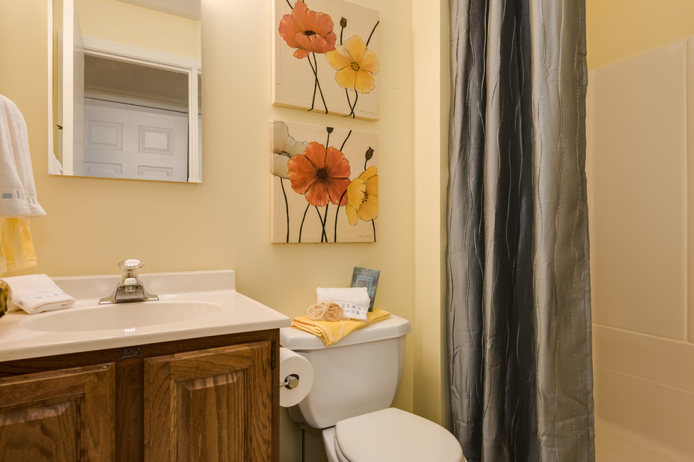 Design ideas for a mid-sized modern bathroom in DC Metro with raised-panel cabinets, dark wood cabinets, an alcove tub, an alcove shower, a two-piece toilet, white tile, yellow walls, laminate floors, an integrated sink, solid surface benchtops and yellow floor.