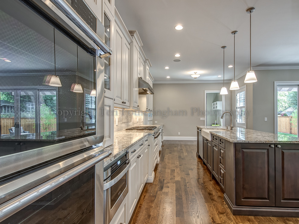 Kitchen - transitional medium tone wood floor kitchen idea in Denver with a farmhouse sink, white cabinets, granite countertops, white backsplash, stainless steel appliances and an island