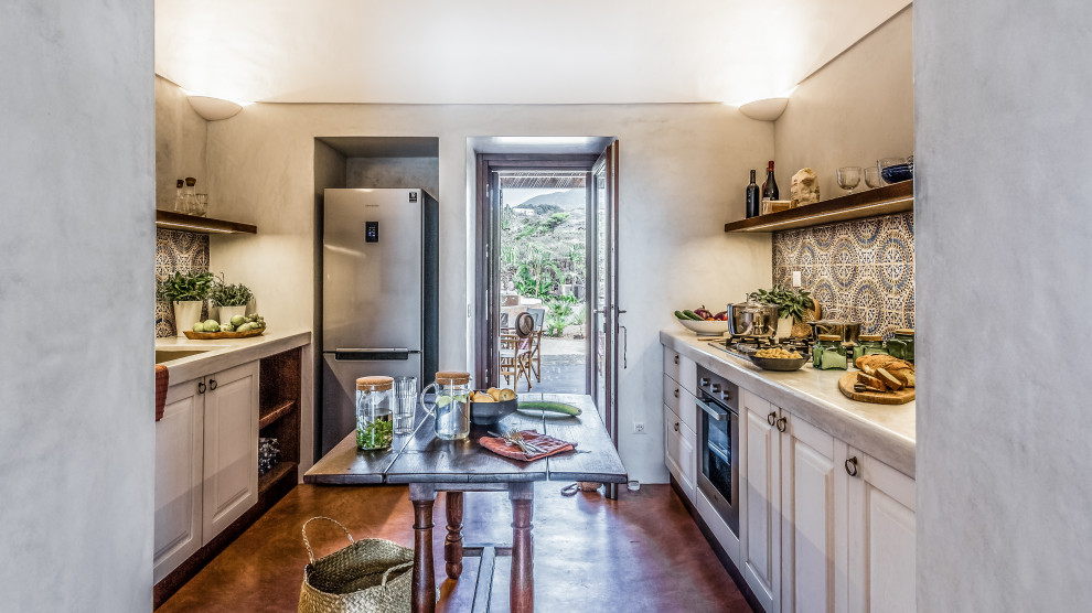 Inspiration for a mediterranean galley separate kitchen in Other with an undermount sink, raised-panel cabinets, white cabinets, multi-coloured splashback, stainless steel appliances, concrete floors, multiple islands, brown floor and grey benchtop.