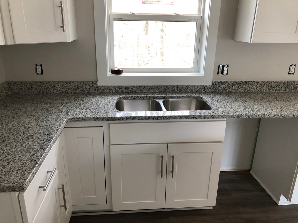 This is an example of a mid-sized contemporary l-shaped open plan kitchen in Grand Rapids with a double-bowl sink, shaker cabinets, white cabinets, granite benchtops, medium hardwood floors, with island, grey floor and grey benchtop.