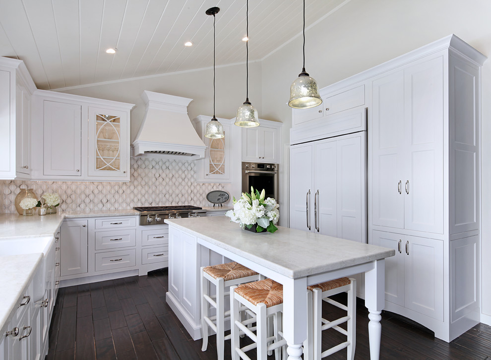 Example of a mid-sized transitional u-shaped dark wood floor enclosed kitchen design in Orange County with a farmhouse sink, beaded inset cabinets, white cabinets, quartzite countertops, white backsplash, glass sheet backsplash, stainless steel appliances and an island