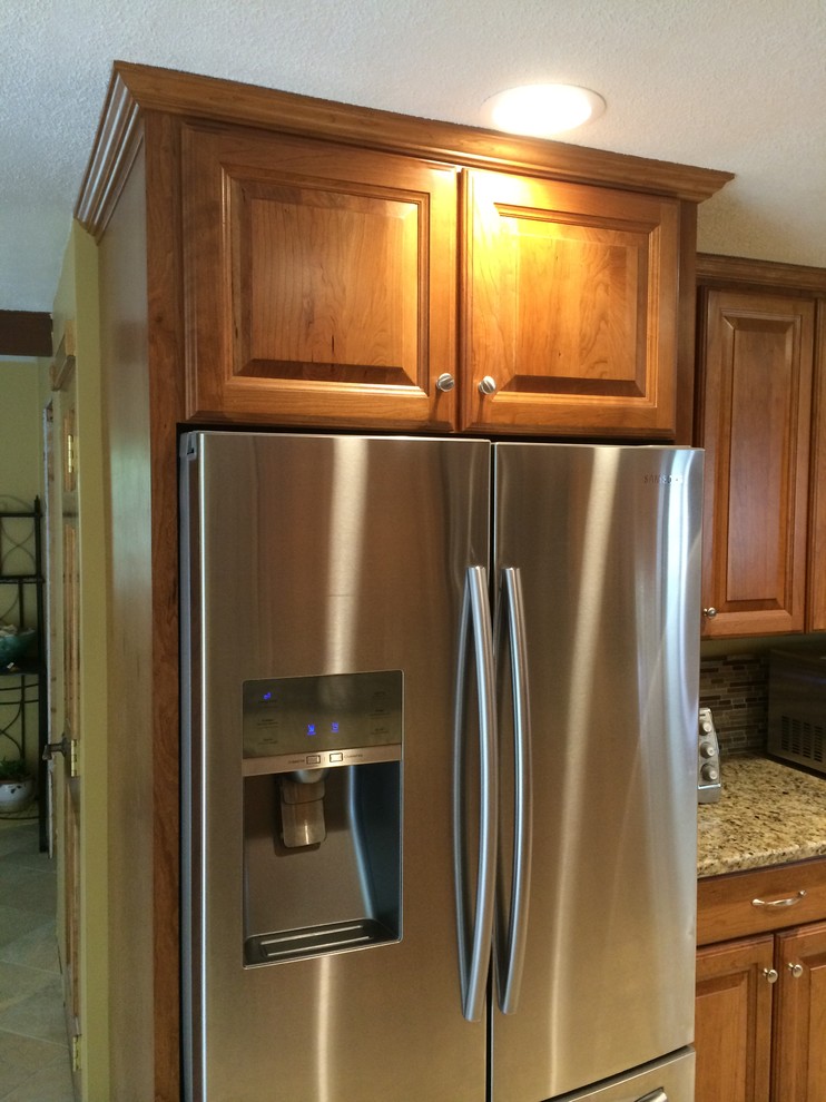 This is an example of a mid-sized traditional u-shaped kitchen pantry in Boston with raised-panel cabinets, medium wood cabinets, granite benchtops, brown splashback, stainless steel appliances, terrazzo floors and a peninsula.