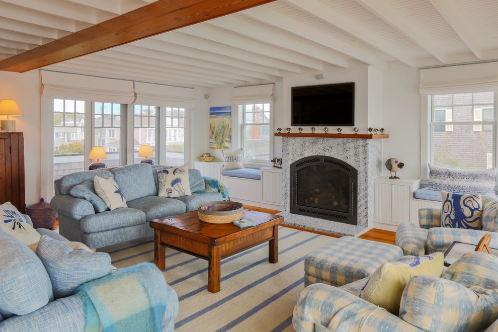 This is an example of a beach style living room in Boston with white walls, medium hardwood floors, a standard fireplace, a tile fireplace surround and a wall-mounted tv.